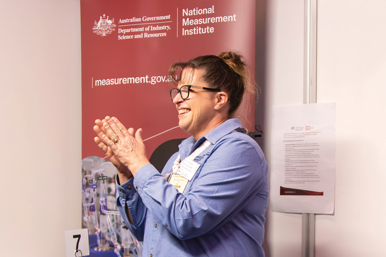 A middle-aged woman is standing at an event booth with banners displaying text and images.