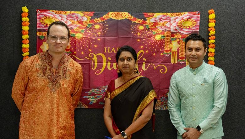 Three people posing in front of a banner at a Diwali celebration