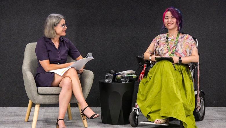 Two women on a stage in front of attendees at an International Day of People with Disability keynote event