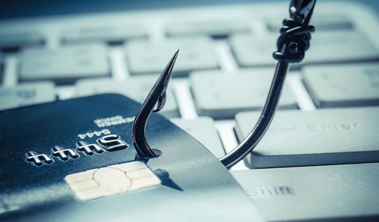 A fishing hook going through a credit card. The credit card is lying on a computer key board. 