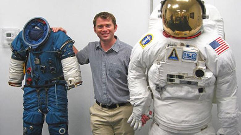 James Waldie poses with NASA Extravehicular Activity suits used for spacewalking.