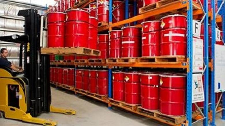 Photo of a worker in a factory operating a forklift and lifting red barrels onto a row of industrial shelving.