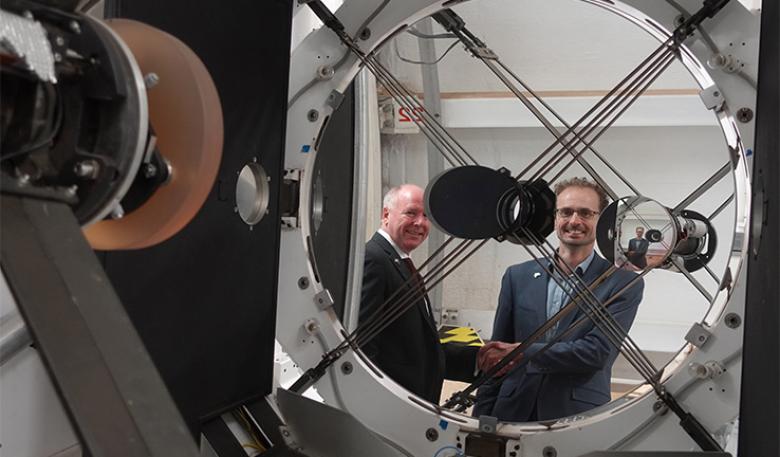 Australian Space Agency and EOS Space Systems leaders shake hands, reflected in the lens of space tracking equipment at the observatory. Australian Space Agency and EOS Space Systems leaders shake hands, reflected in the lens of space tracking equipment at the observatory.