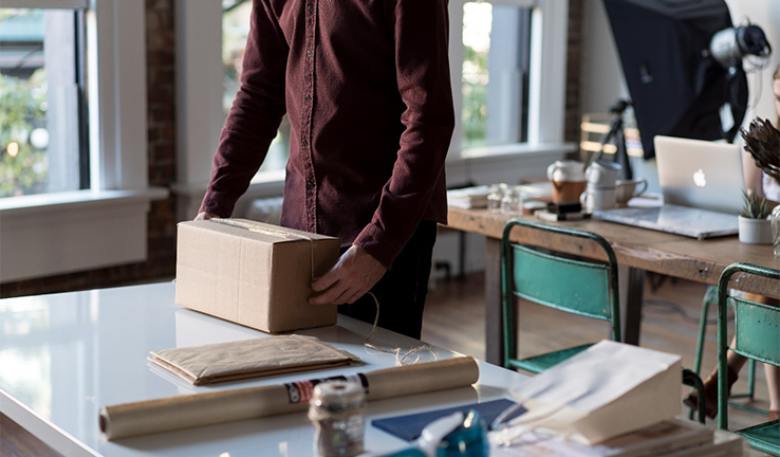 A man standing at a desk about to unwrap a gift.