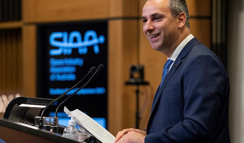 Enrico Palermo at a lectern holding his speech and smiling at the audience. Enrico Palermo at a lectern holding his speech and smiling at the audience. The Space Industry Association of Australia’s (SIAA) logo is on a digital board in the background.