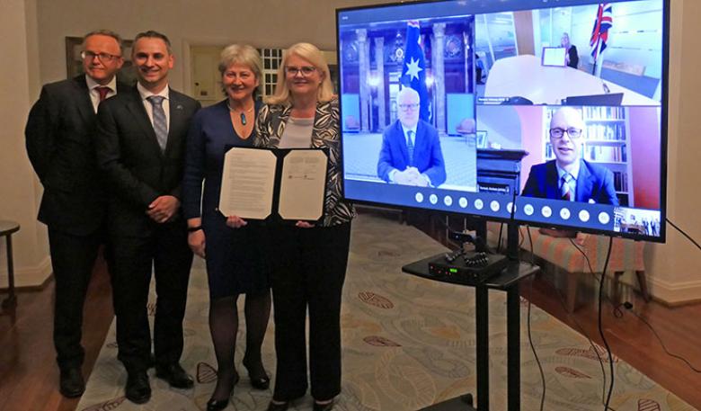 4 people standing in front of a large television, with 3 more people on the screen