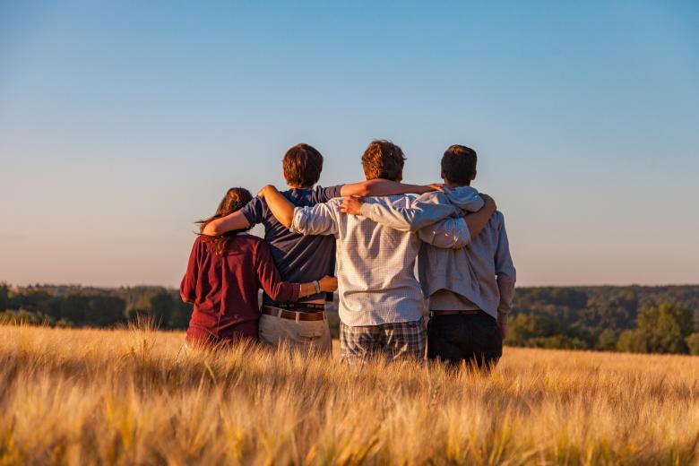 Group of 4 people with their arms around each other in a field.