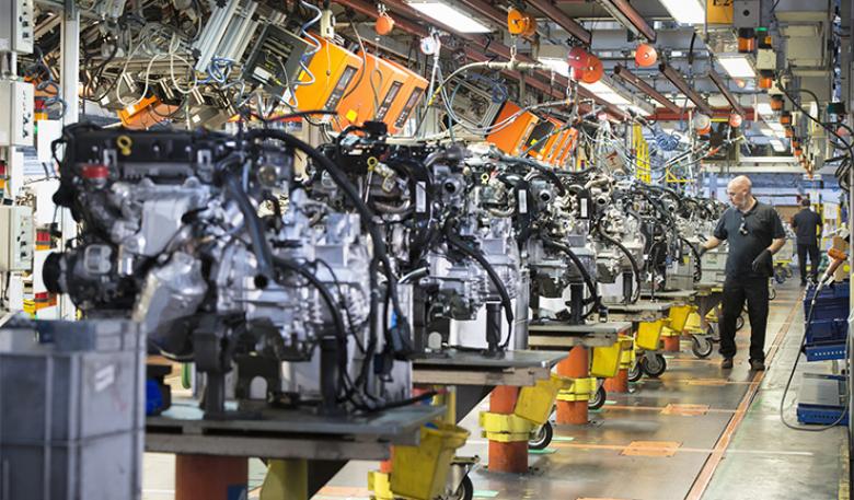 An automotive worker inspects car engines in a factory.