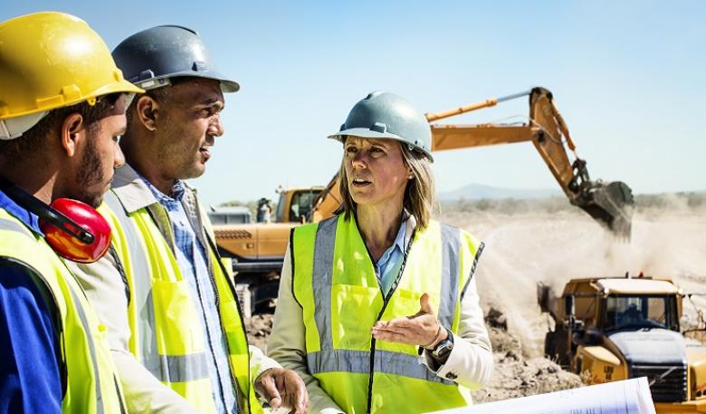 Photo of three miners, a woman and two men, wearing hard hats on a site.