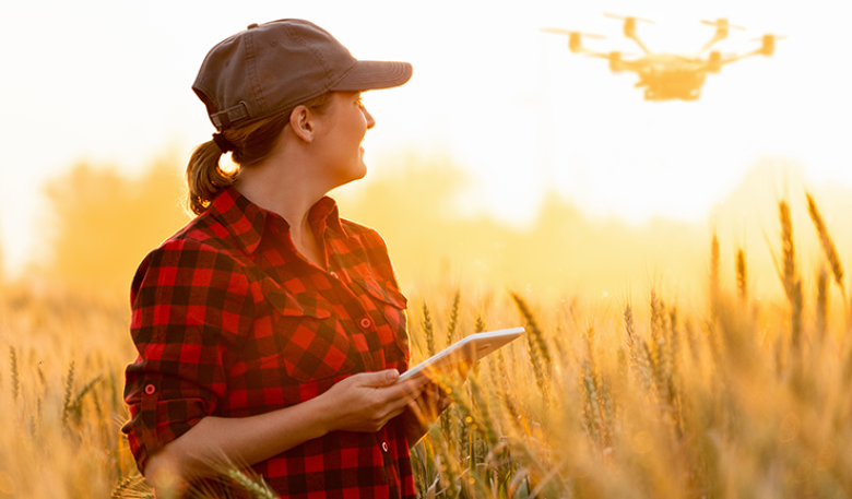 Person standing in a field flying a drone in the sky behind her.