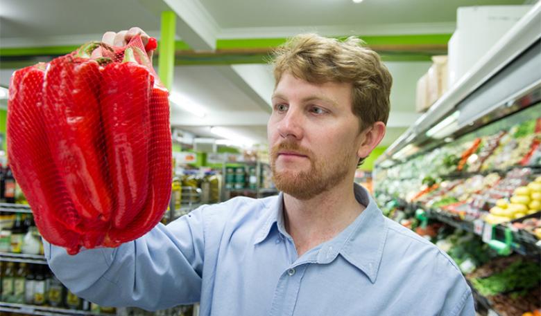 Photo of an inspector holding up a packaged red pepper in a supermarket