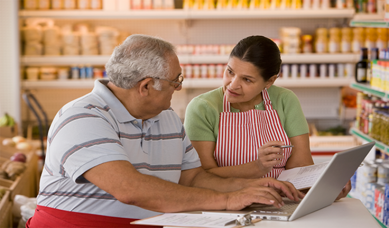 Two people sitting in a shop looking at a laptop. 