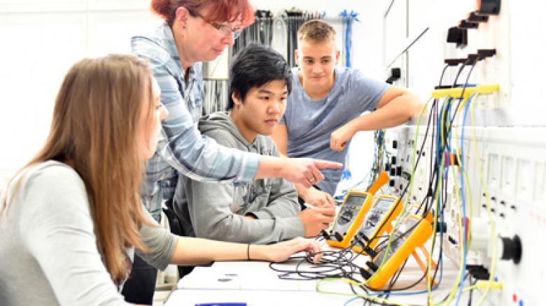 Photo of young students and teacher looking at STEM equipment in a lab.
