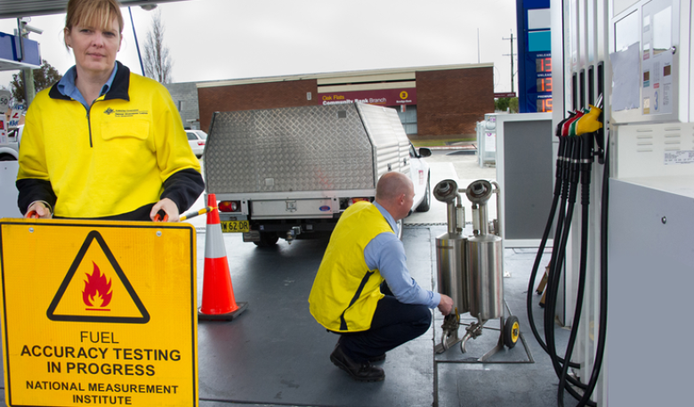 An inspector holds a sign saying fuel accuracy testing in progress at a petrol station.
