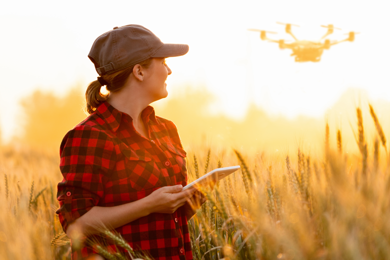 Person standing in a field flying a drone in the sky behind her.