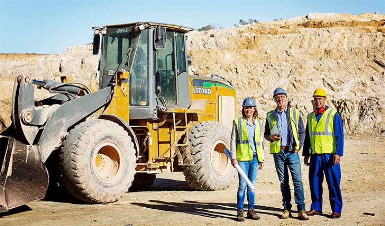 Three people standing in front of earth-moving equipment