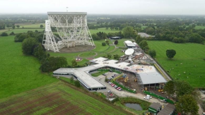 Aerial shot of the SKA head office in Manchester adjacent to a large radio telescope and lush green fields.