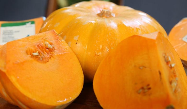 Photo of two cut pieces of orange pumpkin with a whole pumpkin behind them
