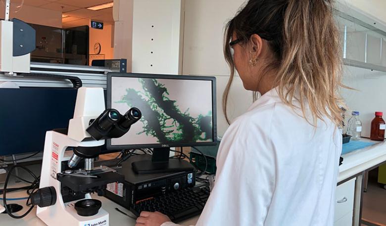A woman in a laboratory coat looking at a computer and microscope.
