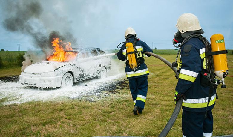 Two firemen wearing breathing apparatus, extinguishing a car fire
