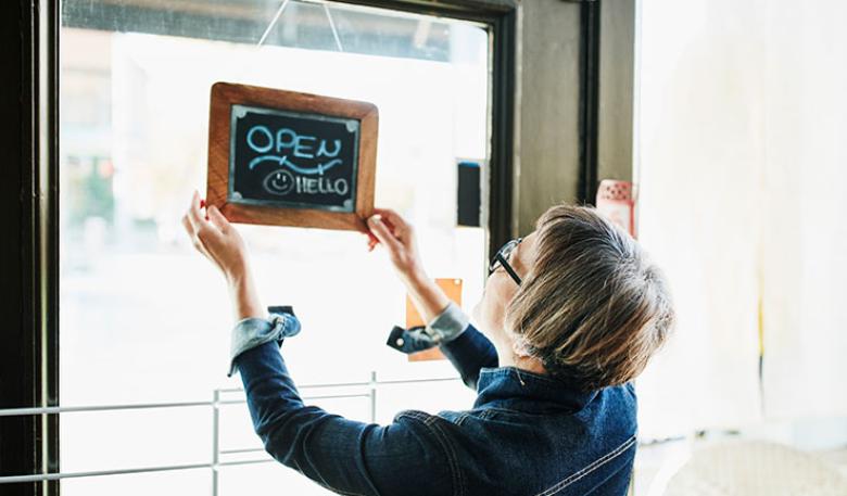 Woman changing a shop sign in the window to ‘open’. 