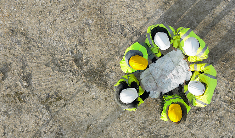 Ariel photo of a group of miners with hard hats looking at a map.