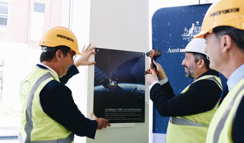 Three men looking at a poster of a satellite