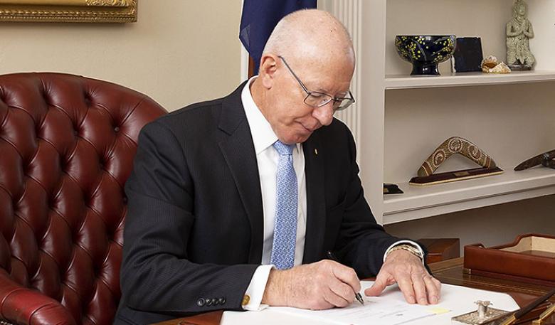 The Governor General of Australia, at a desk, signing papers.
