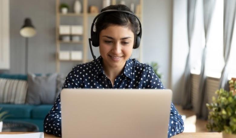  Image of a woman with a headset using her laptop to attend a webinar remotely. 