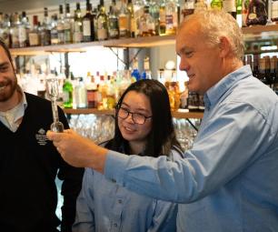 Three people stand in a bar measuring a drink