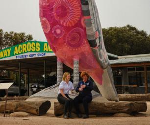 Two people sitting in front of a large sculpture of a galah 