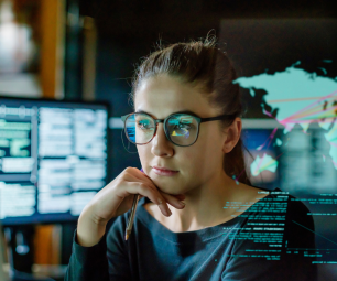 Photo of woman working in front of computer monitors in an office. In front of her, there is a see-through panel displaying a map of the world and other data.
