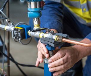 A person in high-visibility workwear adjusts the meter attached to some copper piping