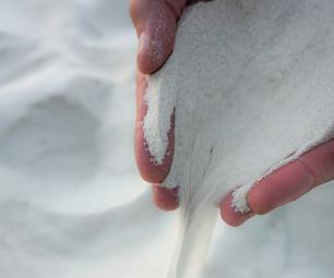 A pair of hands is picking up white silica sand and letting it fall through their fingers