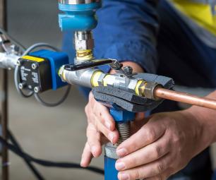 A person in high-visibility workwear adjusts the meter attached to some copper piping