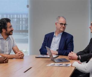 A still from the George Medicines Brandon Capital video showing people sitting around a table talking. 
