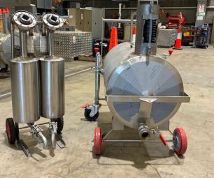 Stainless steel fuel measurement equipment on wheels, including several cylindrical tanks and smaller measurement units, arranged inside a warehouse ready for transport or deployment.