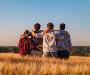 Group of 4 people with their arms around each other in a field.