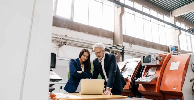 Two professional looking at a laptop in a manufacturing facility.