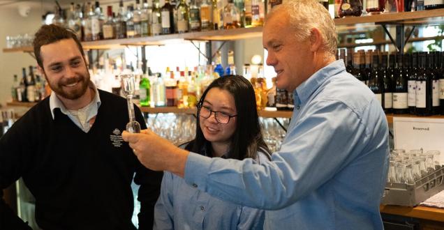 Three people stand in a bar measuring a drink