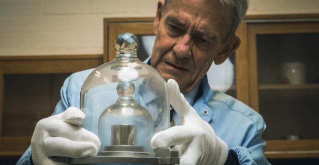 Photo of a man examining a metal weight under glass domes.