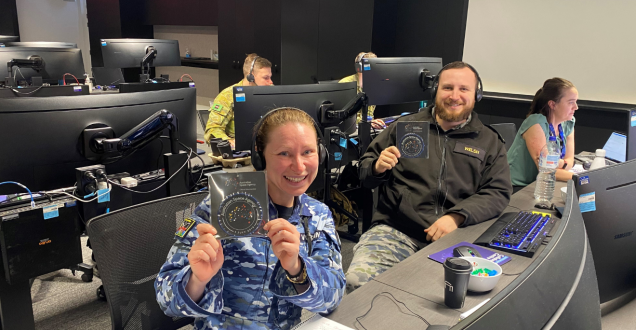 Two people sitting at a desk holding the Australian Space Agency mission patch.