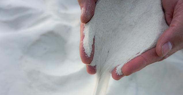 A pair of hands is picking up white silica sand and letting it fall through their fingers