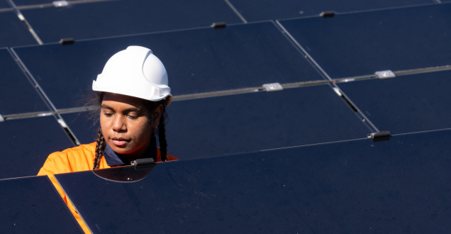 Female Aboriginal Australian technician inspecting photovoltaic panels on solar farm wearing hi-vis workwear