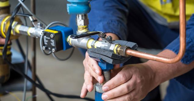 A person in high-visibility workwear adjusts the meter attached to some copper piping