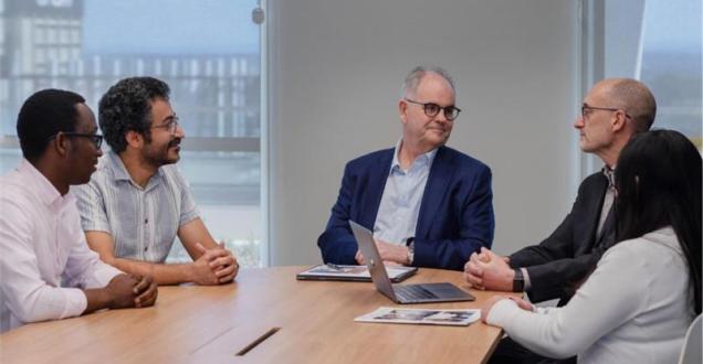 A still from the George Medicines Brandon Capital video showing people sitting around a table talking. 
