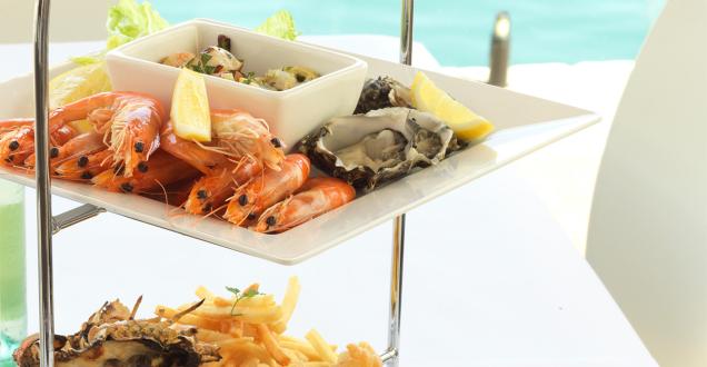 Cooked prawns and fresh oysters arranged on a white platter, served with lemon wedges.