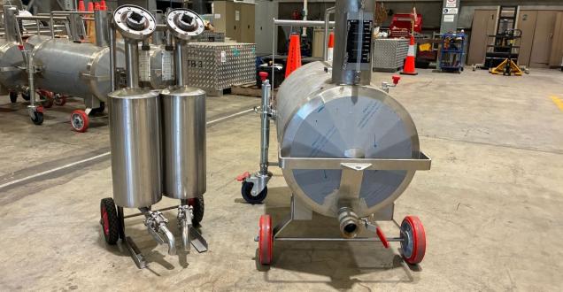 Stainless steel fuel measurement equipment on wheels, including several cylindrical tanks and smaller measurement units, arranged inside a warehouse ready for transport or deployment.