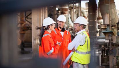 Three people wearing protective clothing meet on an offshore oil and gas facility