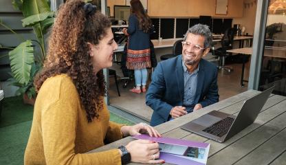 A businessman and women have a conversation at a table over a laptop. 